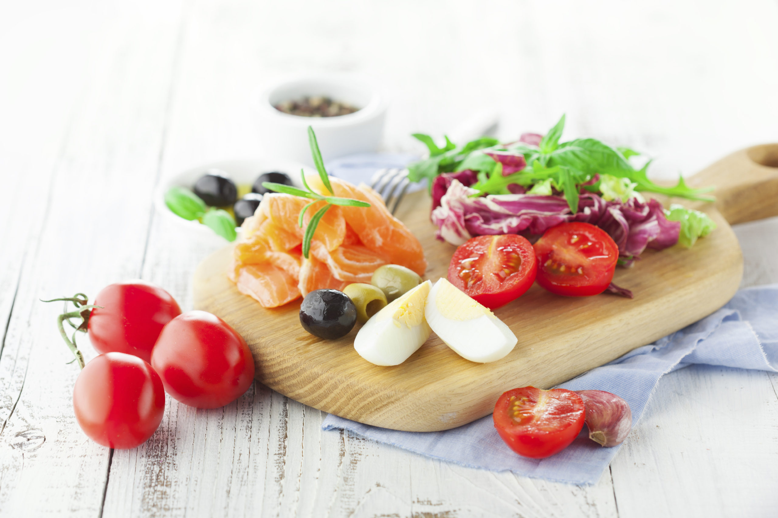Ingredients for salad with salmon, cherry tomatoes and lettuce on a wooden chopping board on rustic white background, selective focus